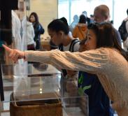 A woman leaning over a glass display, pointing at something out of frame.