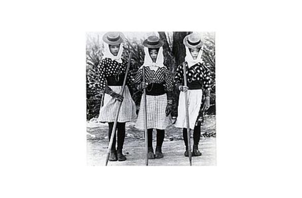 Black and white historical photograph of three women in plantation clothing wearing hats and holding poles